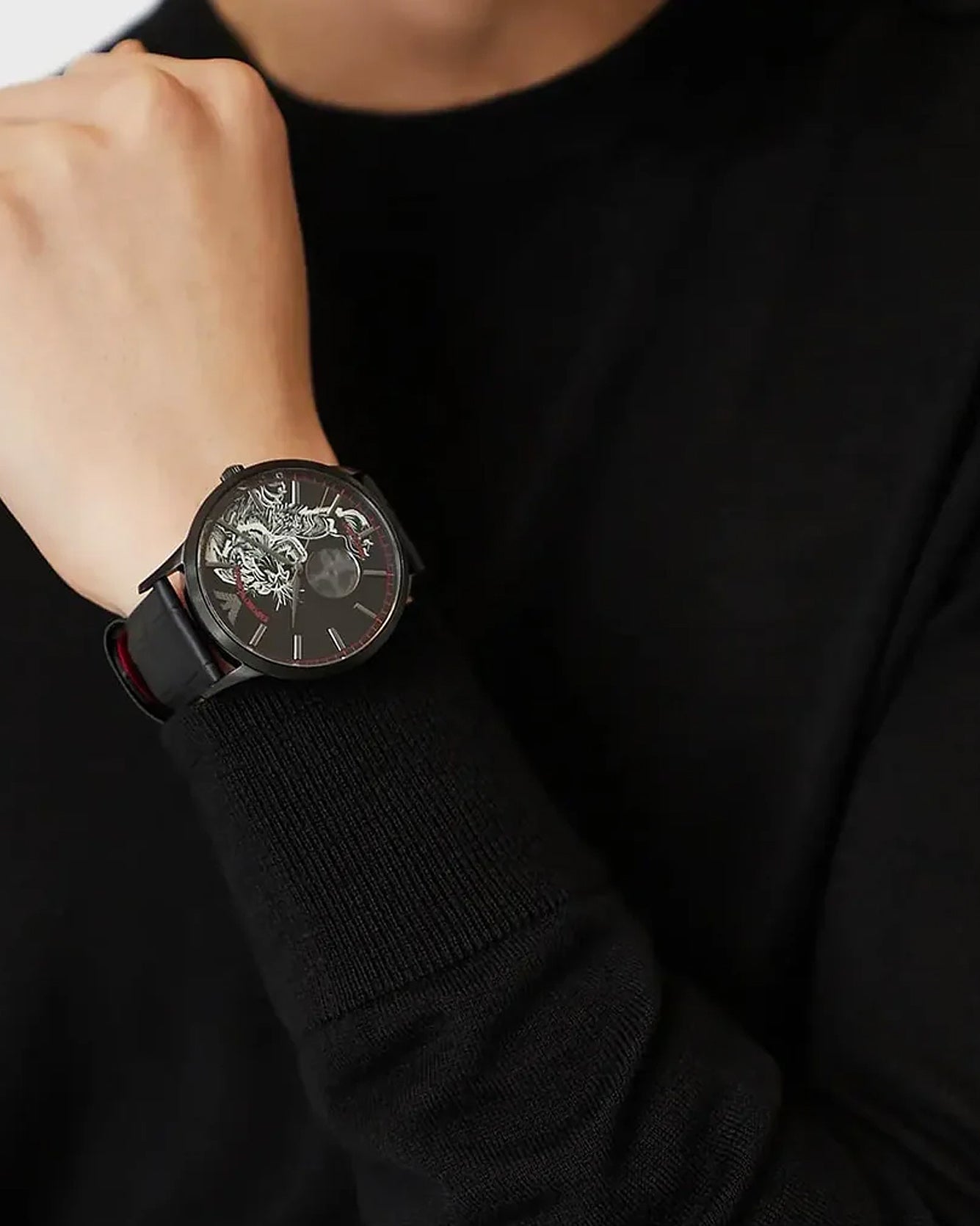 Person wearing a black wristwatch with intricate design on a black background